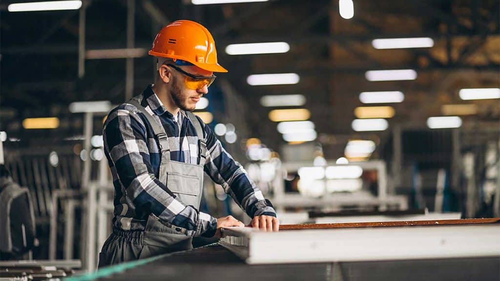 Safe worker in industrial manufacturing, wearing safety gear and inspecting equipment at factory.