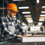 Safe worker in industrial manufacturing, wearing safety gear and inspecting equipment at factory.